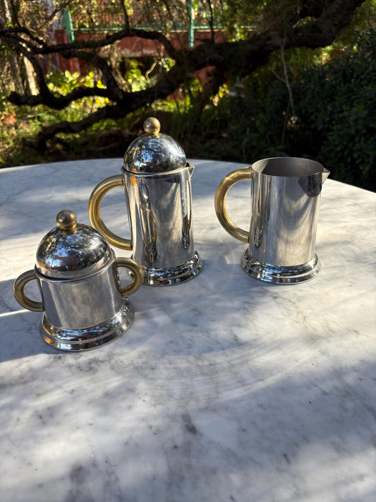 May include: A set of three silver and gold serving pieces. The pieces include a creamer, a sugar bowl, and a pitcher. The pieces are all polished and have a shiny finish.
