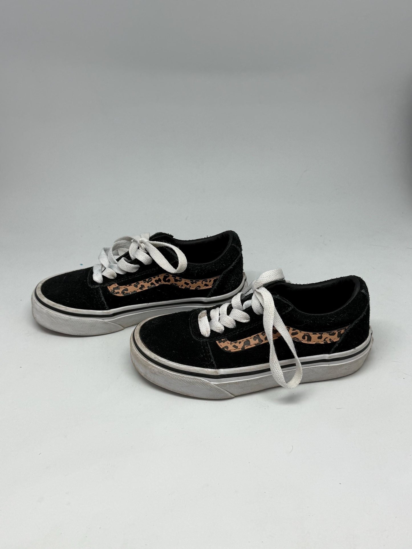 May include: A pair of black trainers with white laces and a white sole. Each shoe has a tan and brown leopard print design on the side. These are children's shoes.