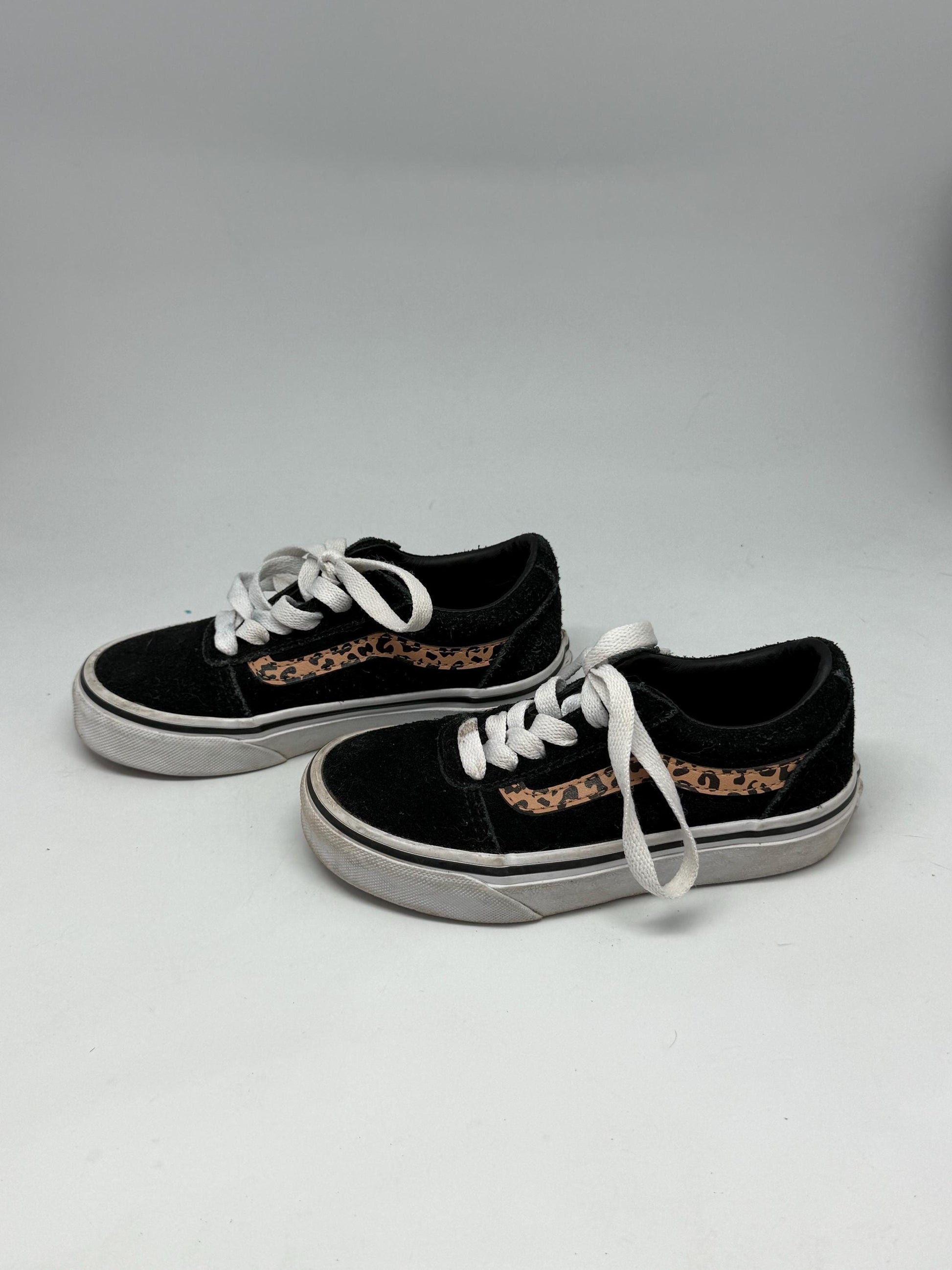 May include: A pair of black trainers with white laces and a white sole. Each shoe has a tan and brown leopard print design on the side. These are children's shoes.