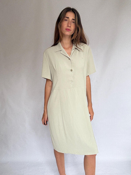 May include: A pale green dress with a collared neckline and short sleeves. It features a button-down front and a knee-length hem. The dress has a tailored silhouette and is made from a lightweight fabric. The design is simple and classic, suitable for various occasions.