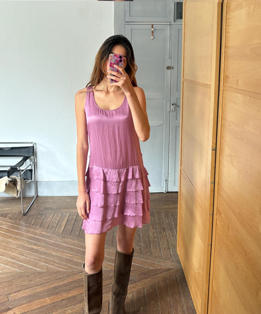 May include: A dusty rose dress with a layered, ruffled skirt. The dress features a scoop neckline and is sleeveless. The model is wearing brown knee-high boots. The dress is made of a soft, flowing fabric.