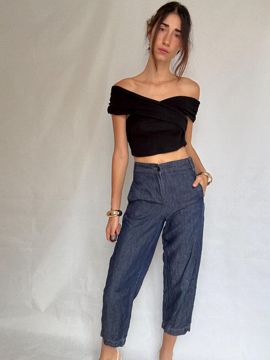 May include: A black, off-the-shoulder top and high-waisted, dark-wash denim trousers. The trousers have a classic fit with a button closure and pockets. The outfit is accessorized with gold bangles.